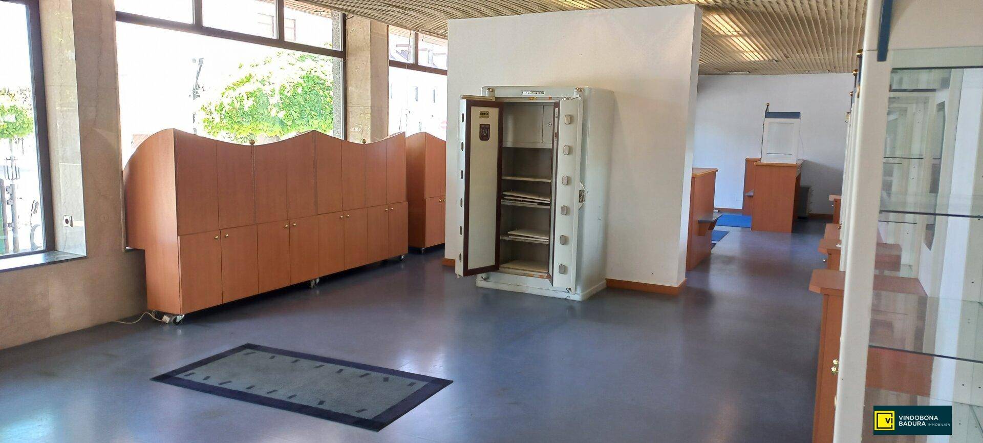 Innenraum eines Geschäfts mit einem geöffneten Tresor, Holzschränken und einem Teppich auf dem dunklen Boden.