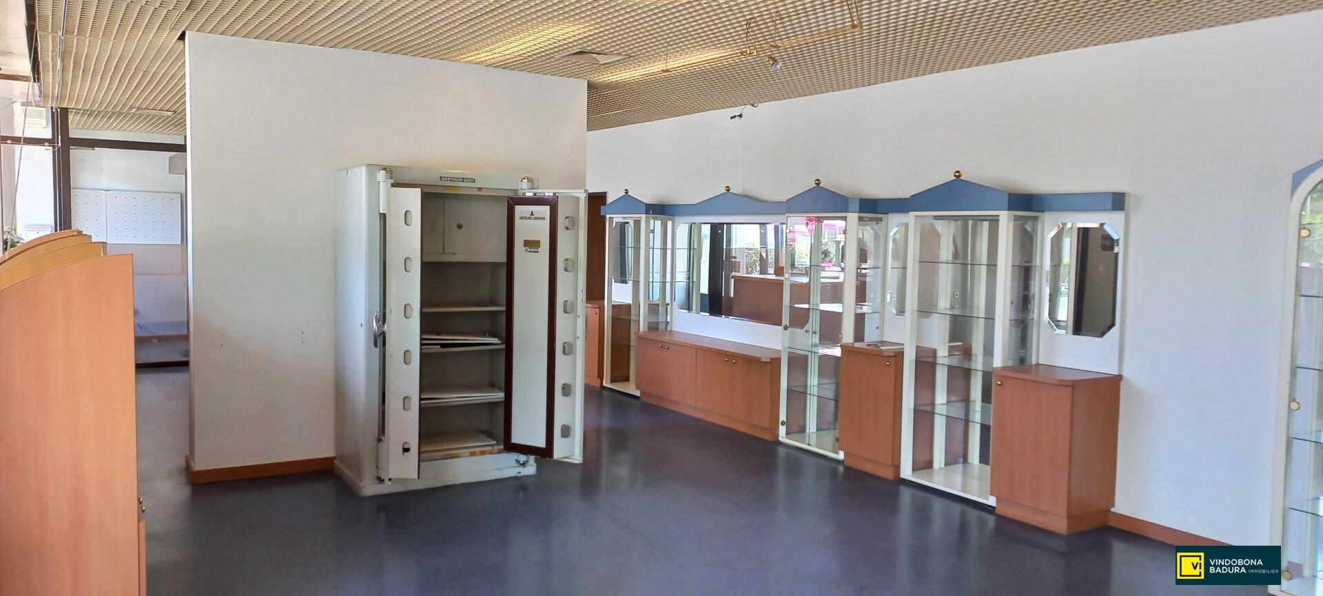 Innenansicht eines Ladenlokals mit einem großen Tresor und mehreren Vitrinen für Ausstellungszwecke und dunklem Boden.