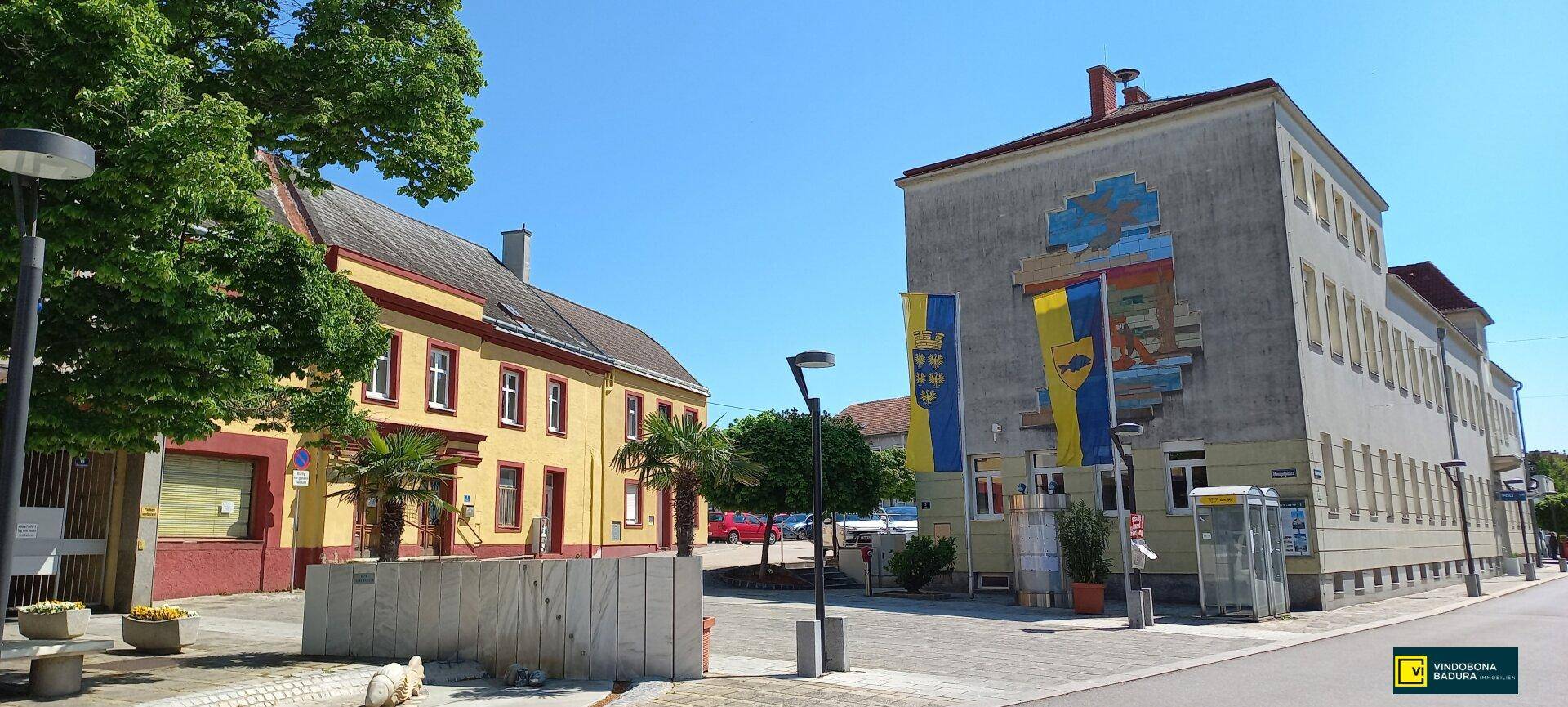 Historische Gebäude entlang einer Straße unter blauem Himmel, umgeben von Bäumen und Grünflächen in der Stadt.