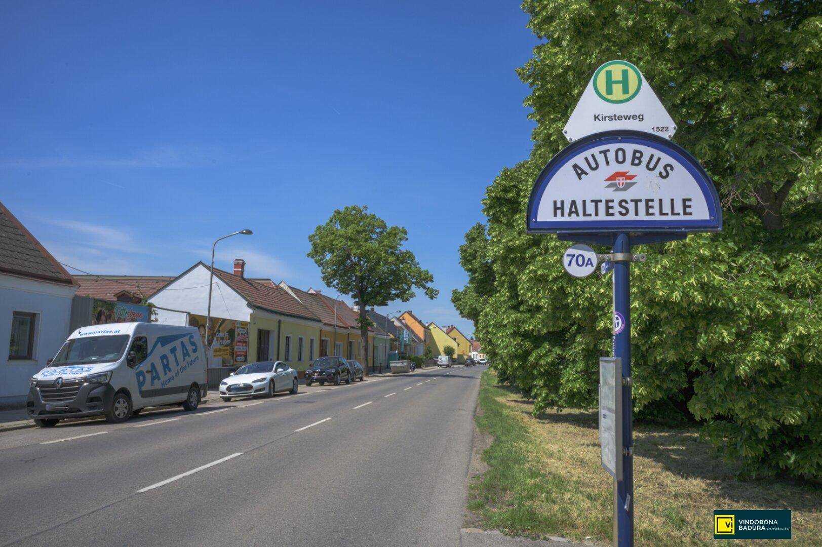 Ländliche Straße mit Bushaltestelle und traditionellen Häusern unter klarem Himmel.