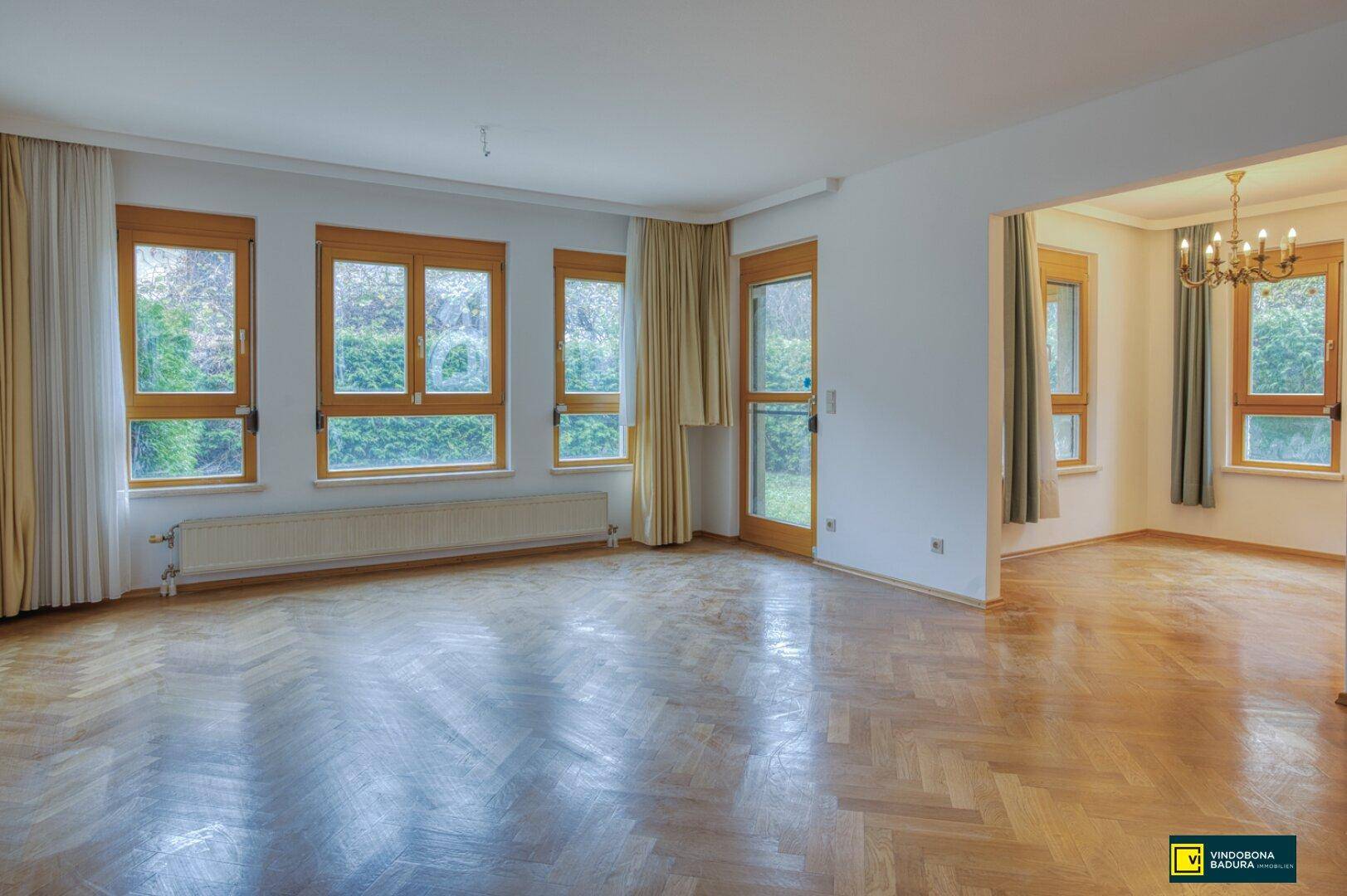 Helles Wohnzimmer mit Fischgrätparkettboden, großen Fenstern und Blick ins Grüne.