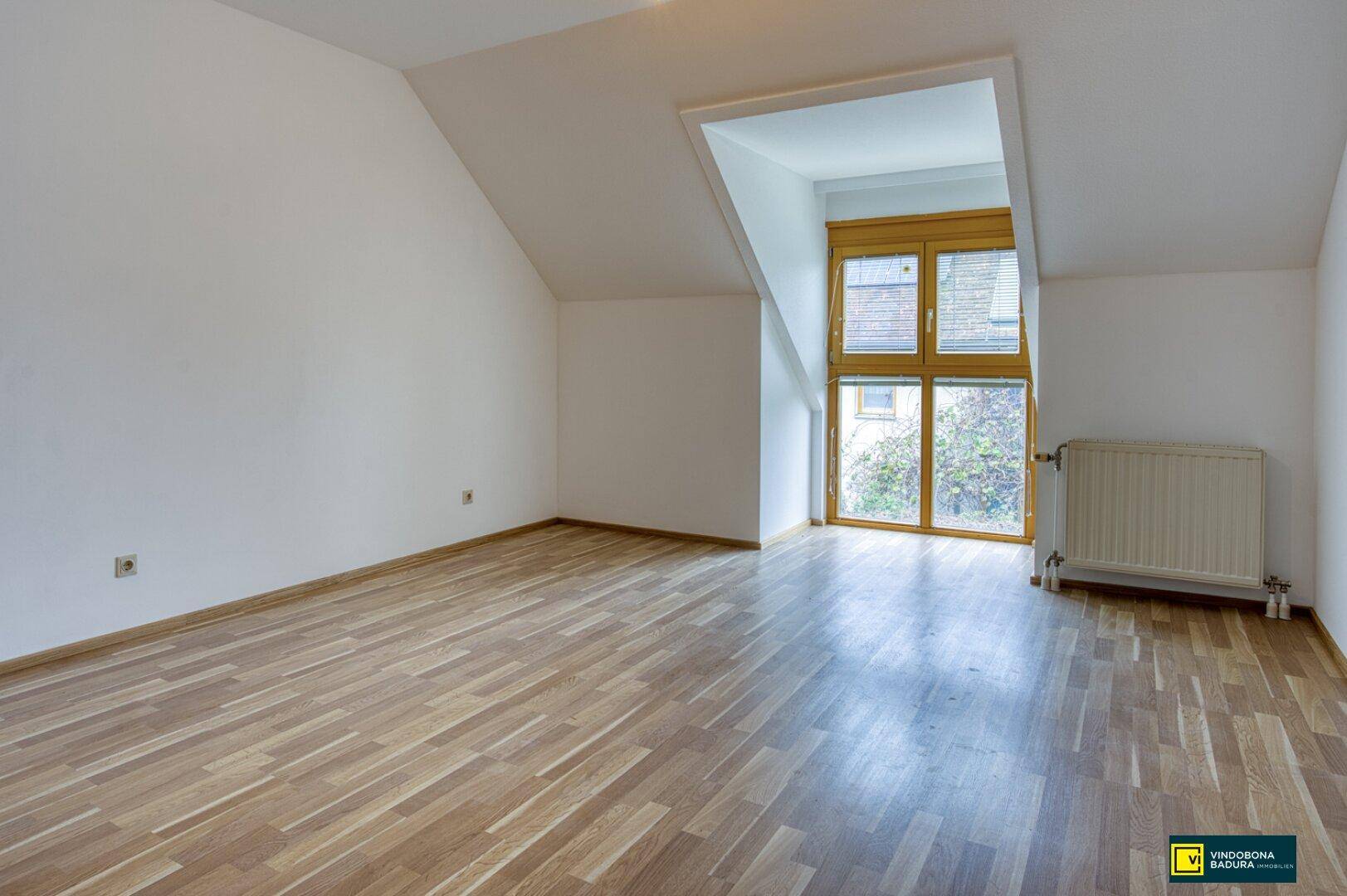 Heller Raum im Dachgeschoss mit Schrägdecke und großem Fenster, ideal als Schlafzimmer.