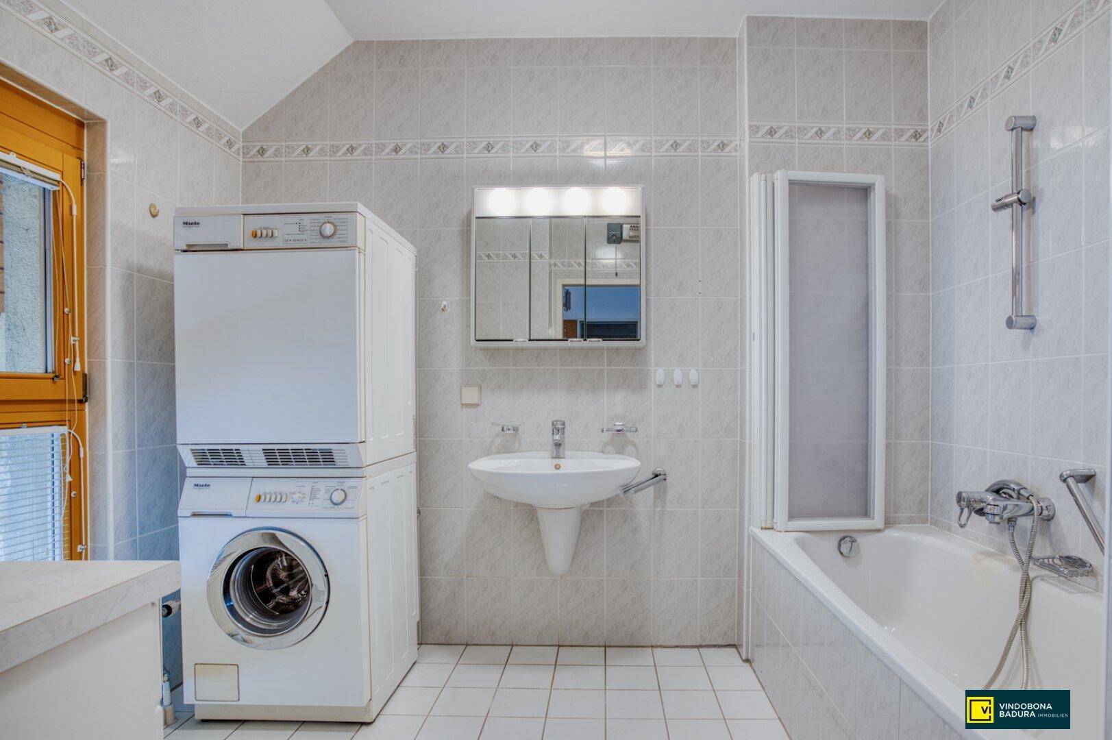 Badezimmer mit Badewanne, Waschbecken, Spiegelschrank und gestapelter Waschmaschine/Trockner.