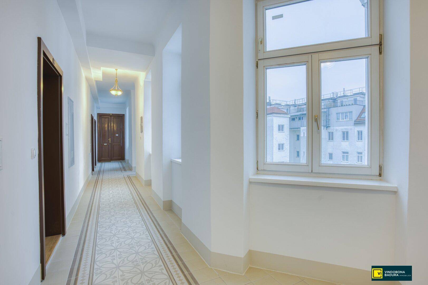 Heller Flur mit gemusterten Fliesen, hohen Decken und einem Fenster mit Blick auf die Stadt.