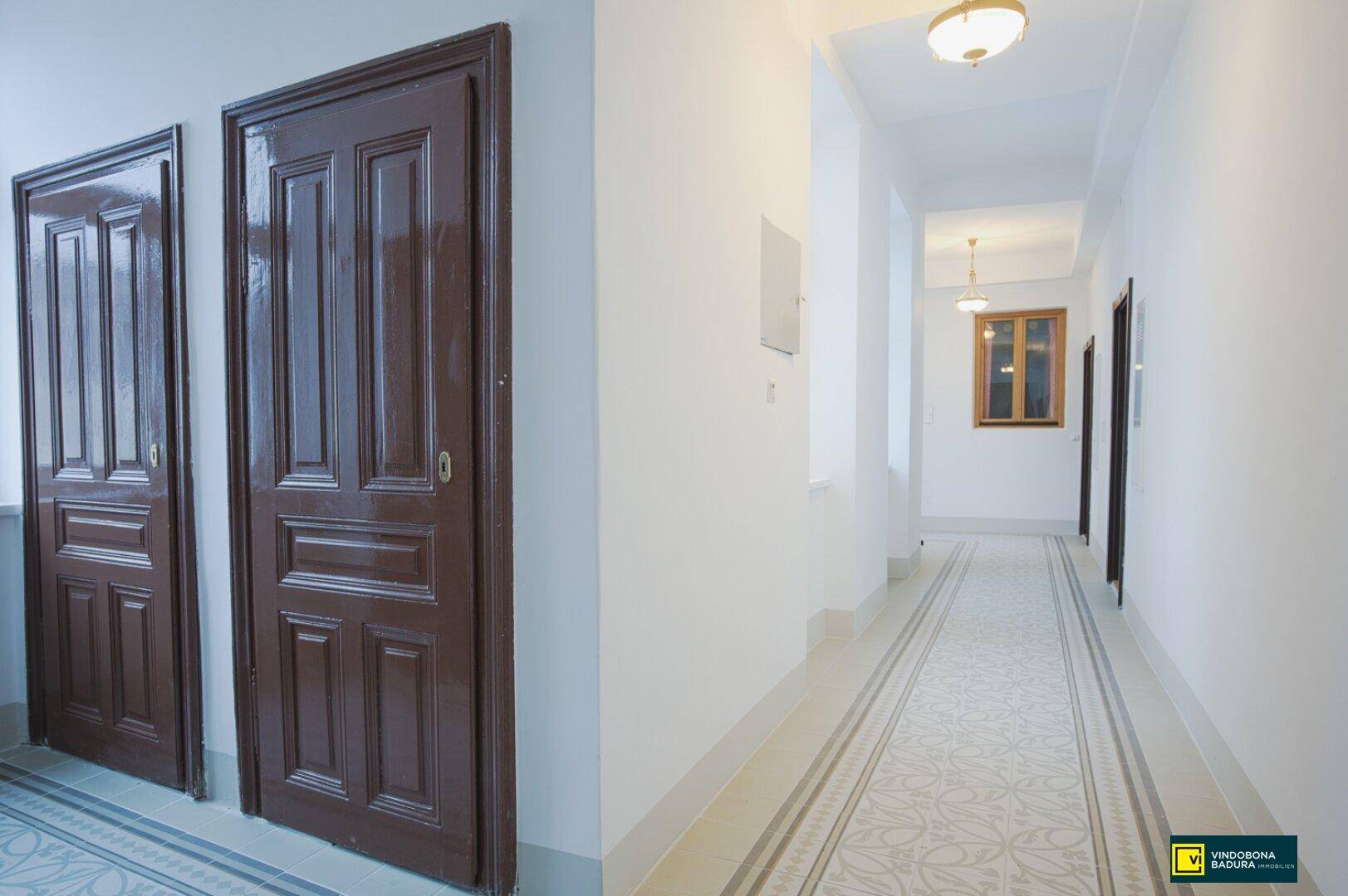 Langer, heller Flur mit gemusterten Fliesen und mehreren Holztüren, der zu verschiedenen Wohnbereichen führt.