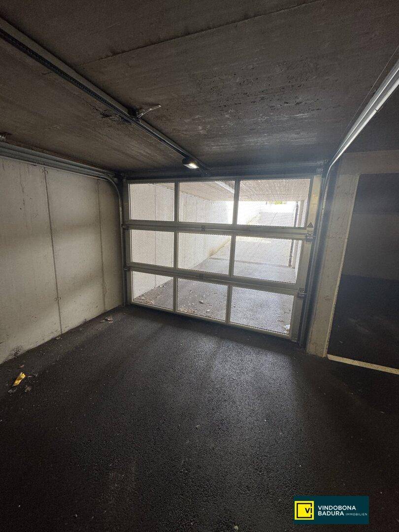 Garagenstellplatz mit geöffnetem Tor, das den Blick auf die Zufahrtsrampe nach draußen freigibt.