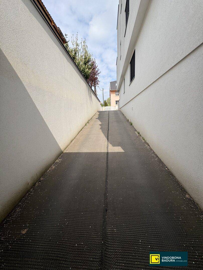 Steile Zufahrtsrampe zwischen zwei Gebäuden, die den Zugang zur Immobilie ermöglicht.