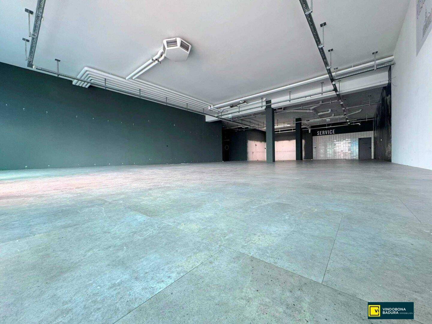 Großer, leerstehender Verkaufsraum mit modernem Bodenbelag und sichtbaren Installationen an der Decke.