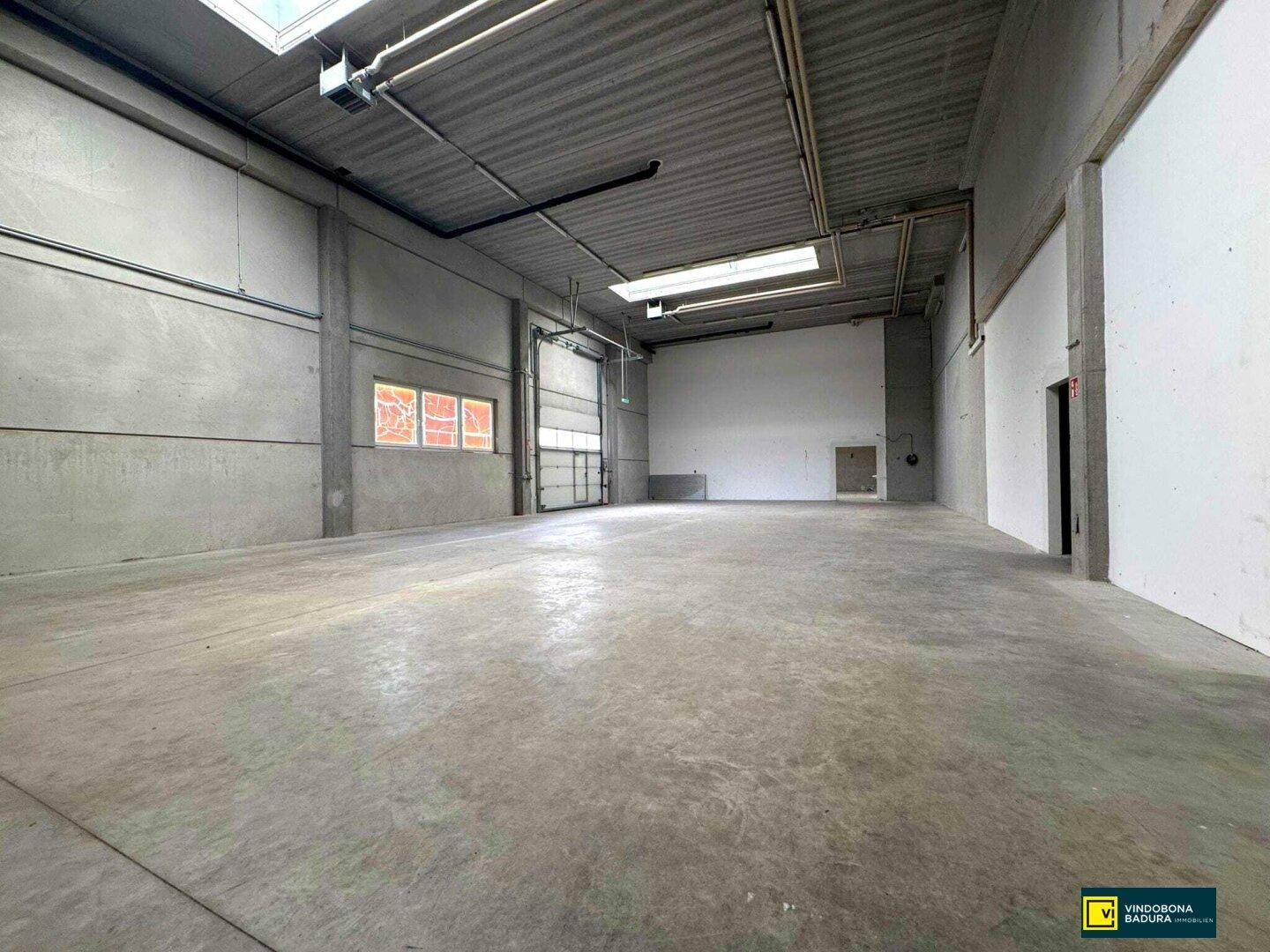 Geräumige Lagerhalle mit Betonboden, Rolltor und hohen Decken, bereit zur Nutzung.