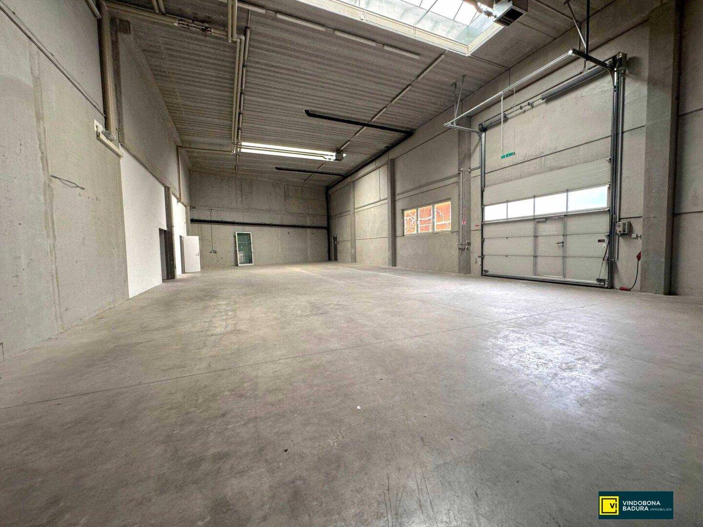 Geräumige Lagerhalle mit hohen Decken, Betonboden und großem Rolltor für Anlieferungen.