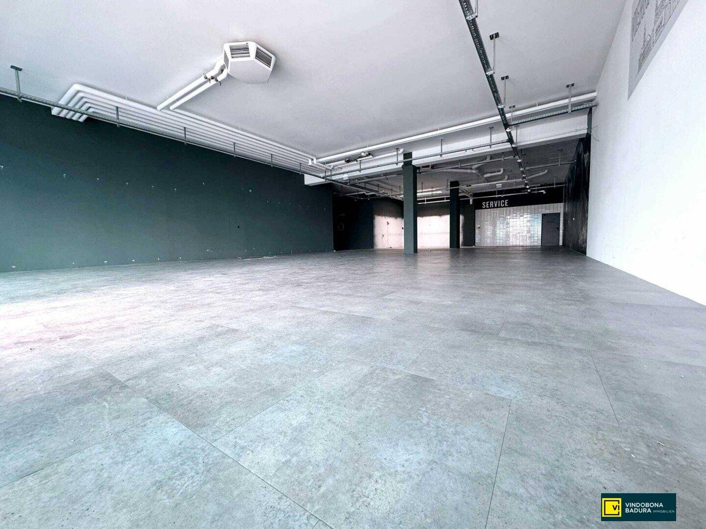 Großer, leerstehender Verkaufsraum mit modernem Bodenbelag und sichtbaren Installationen an der Decke.
