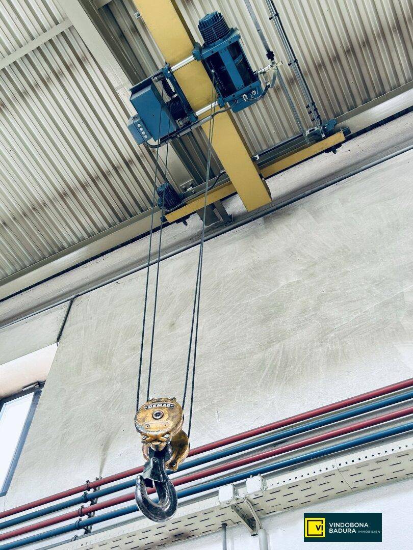 Detailaufnahme der Krananlage mit Haken und Seilen unter der hohen Decke des Industrieraums.