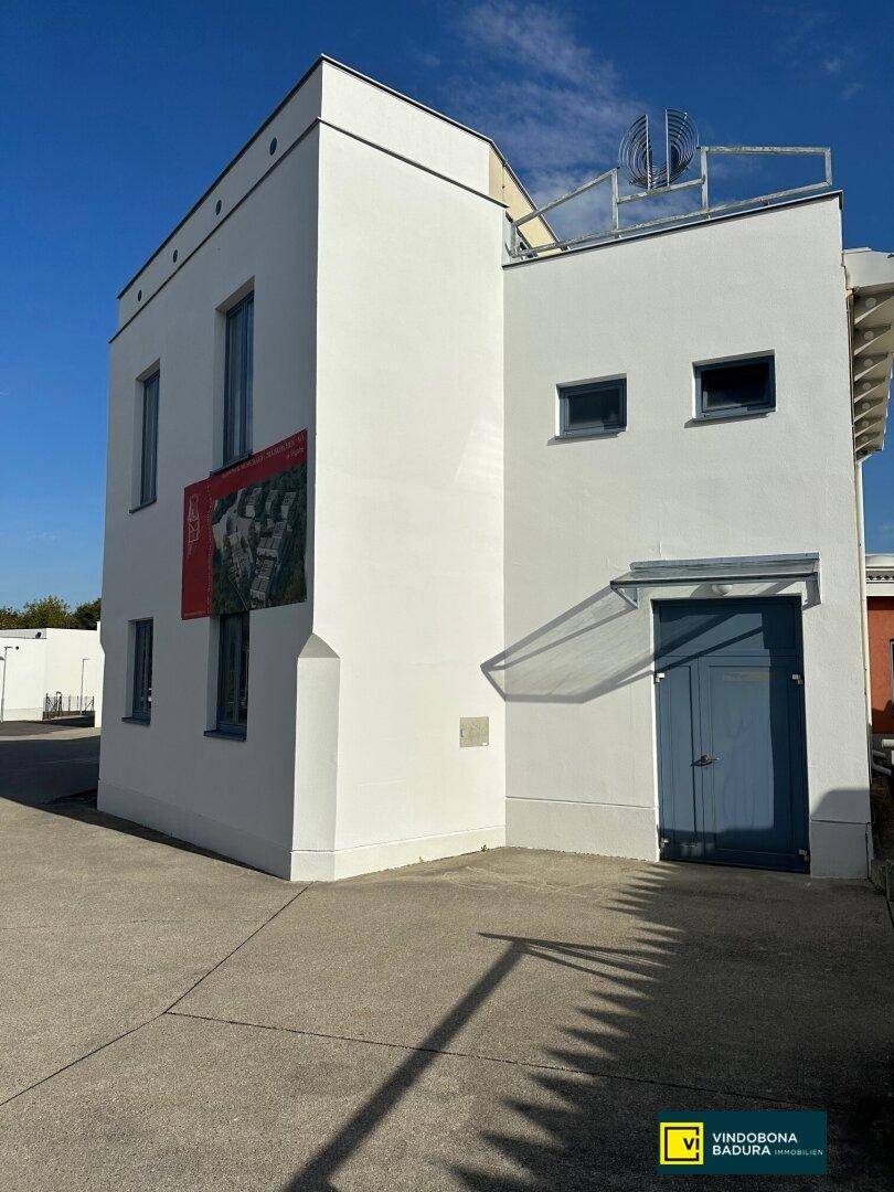 Seitenansicht des modernen Gebäudes mit weißer Fassade und blauen Türen unter klarem Himmel.