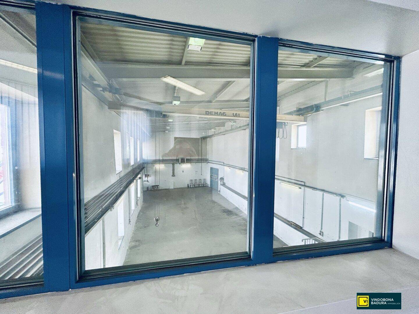 Blick durch große Fenster von einem Flur in den geräumigen Industrie- oder Lagerraum.