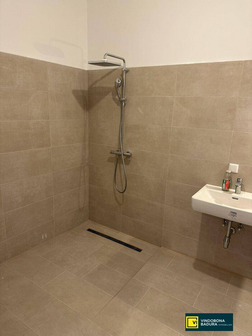 Modernes Badezimmer mit begehbarer Dusche, beigefarbenen Fliesen und einem einzelnen Waschbecken.