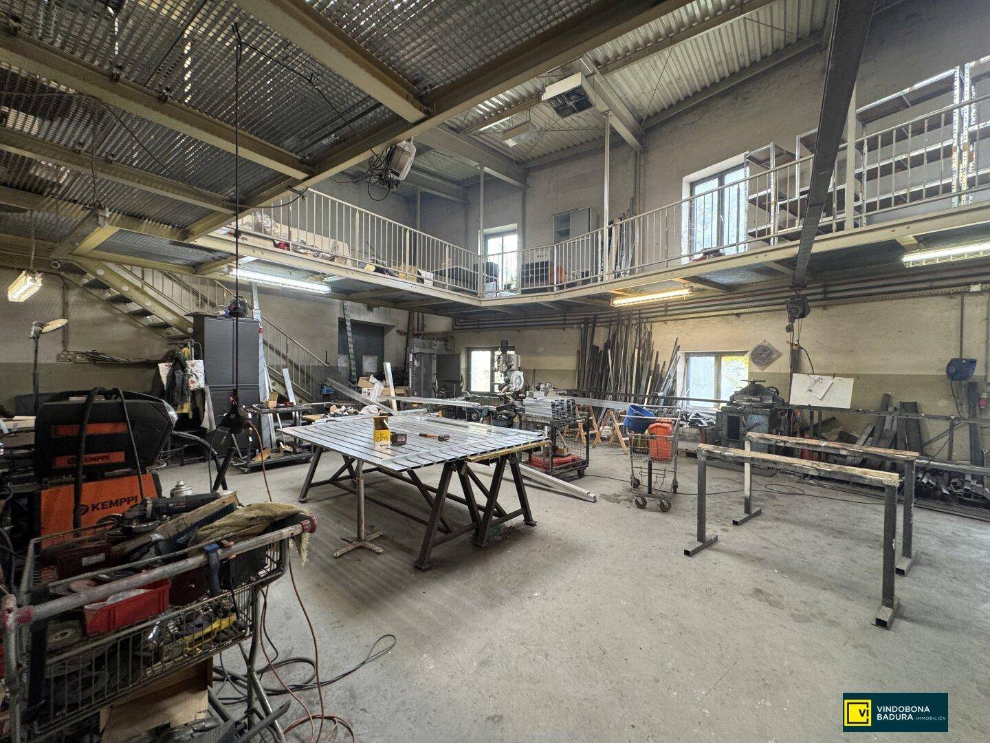 Großer Werkstattbereich mit hoher Decke, Zwischengeschoss und verschiedenen Arbeitsmaterialien.