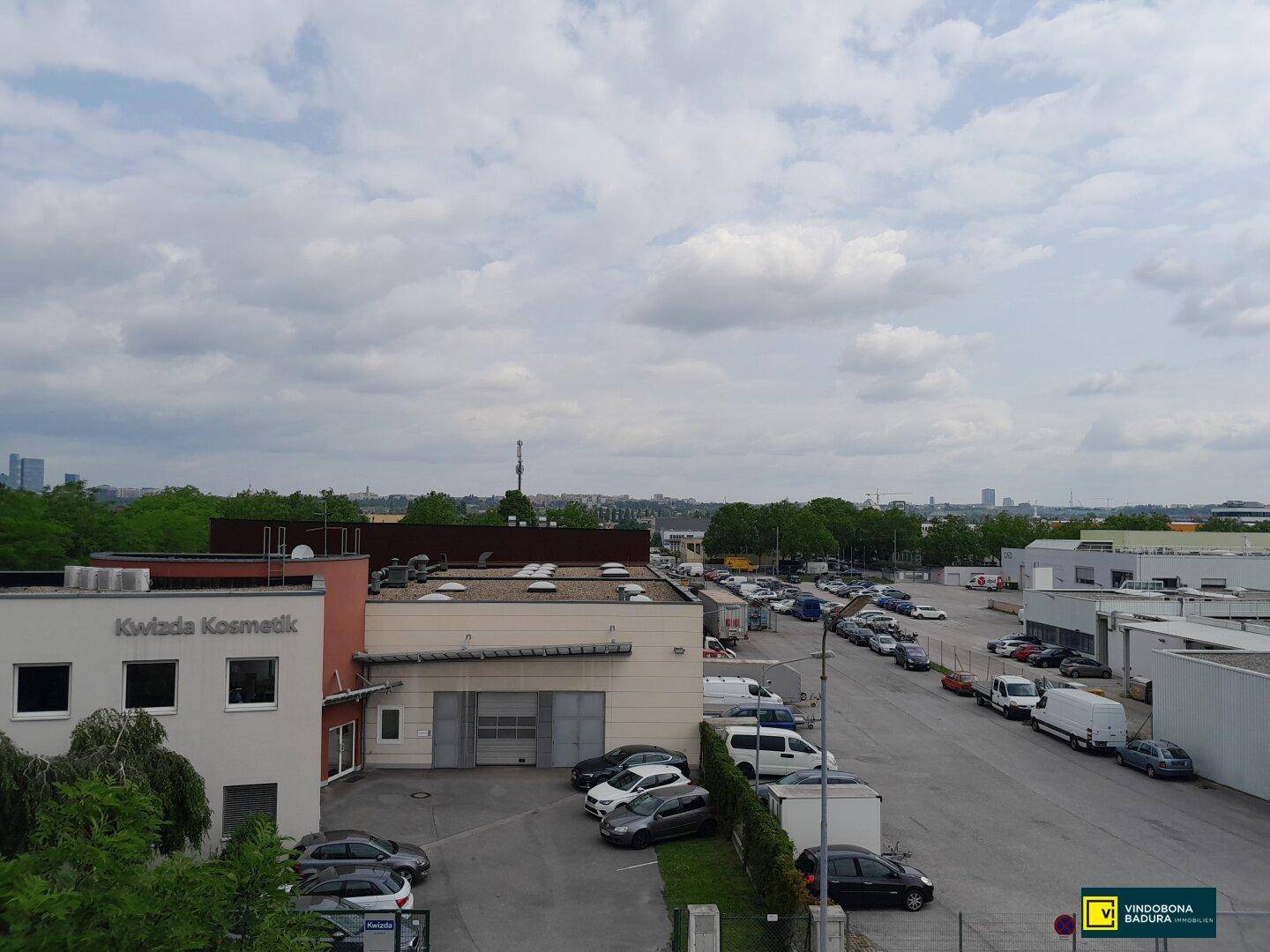 Außenansicht eines Gewerbegebiets mit zahlreichen Parkplätzen und umliegenden Gebäuden unter bewölktem Himmel.