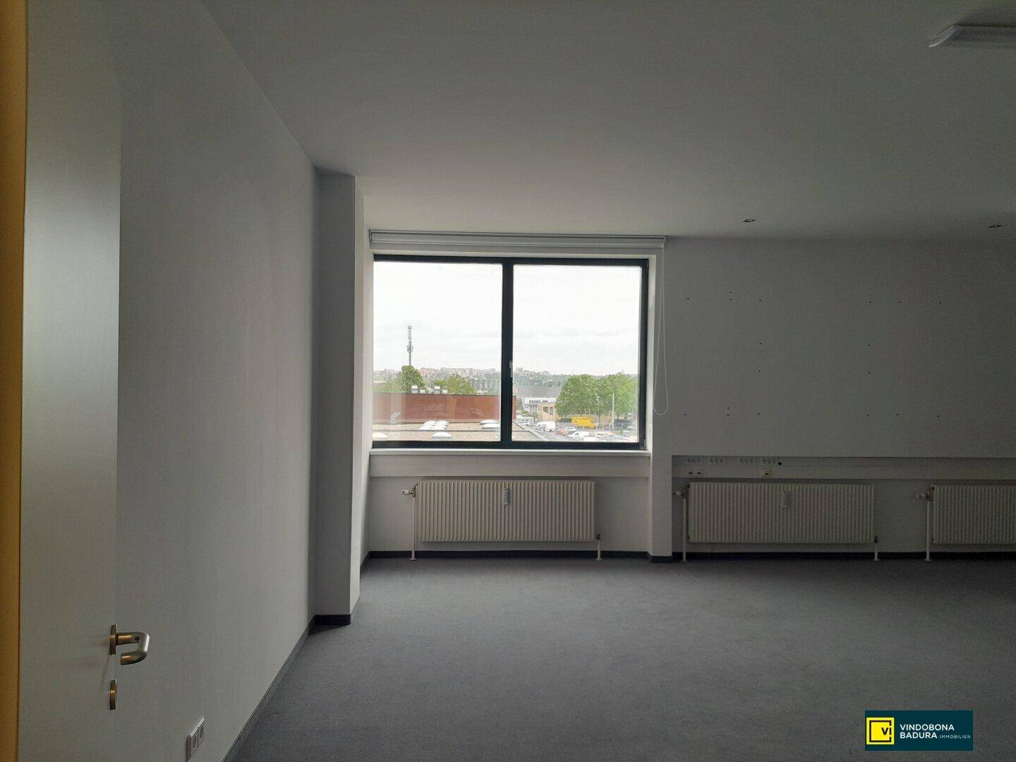 Heller Büroraum mit großem Fenster, Heizkörpern und Teppichboden, bietet eine weite Aussicht.