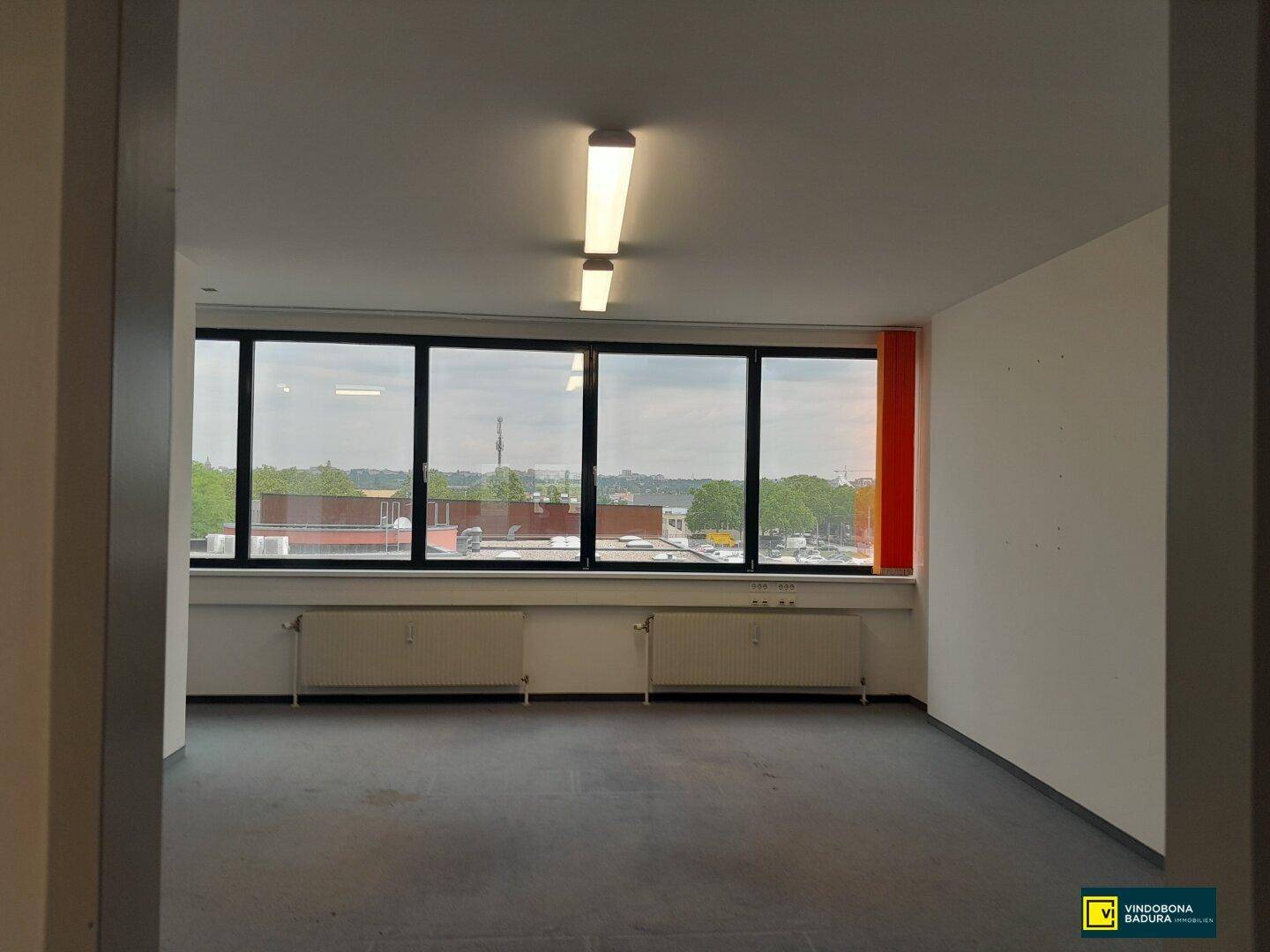 Geräumiger Büroraum mit großen Fenstern, die viel Tageslicht hereinlassen und eine weite Aussicht bieten.