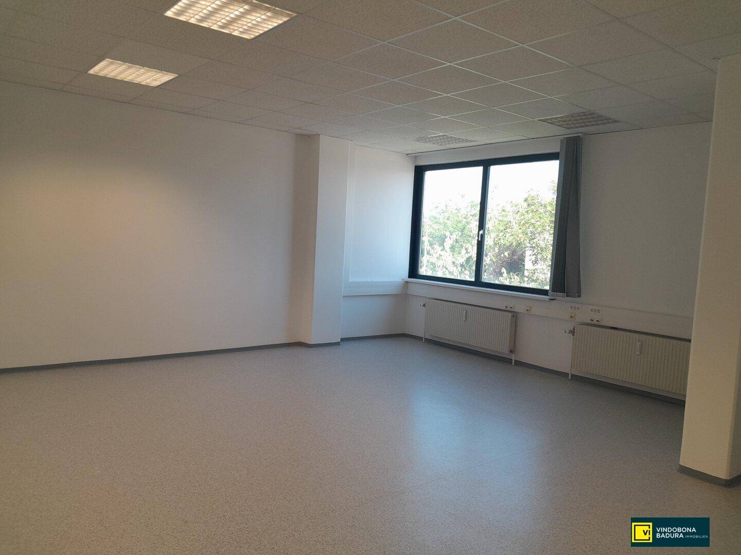 Moderner Büroraum mit großen Fenstern, die viel Tageslicht hereinlassen und eine angenehme Arbeitsatmosphäre schaffen.