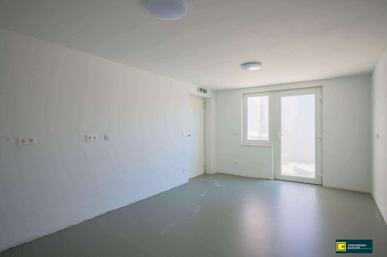Heller Raum mit grauem Vinylboden und einer Tür, die zu einem Außenbereich führt.