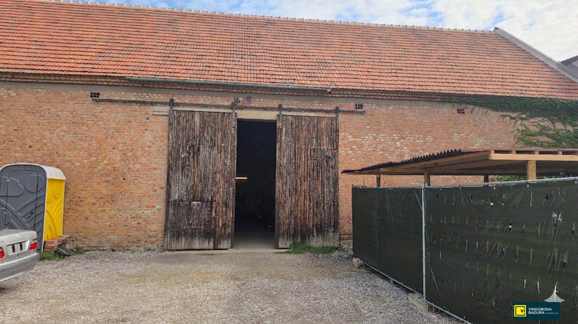Außenansicht eines alten Backsteingebäudes mit roten Ziegeln und großen hölzernen Scheunentoren.