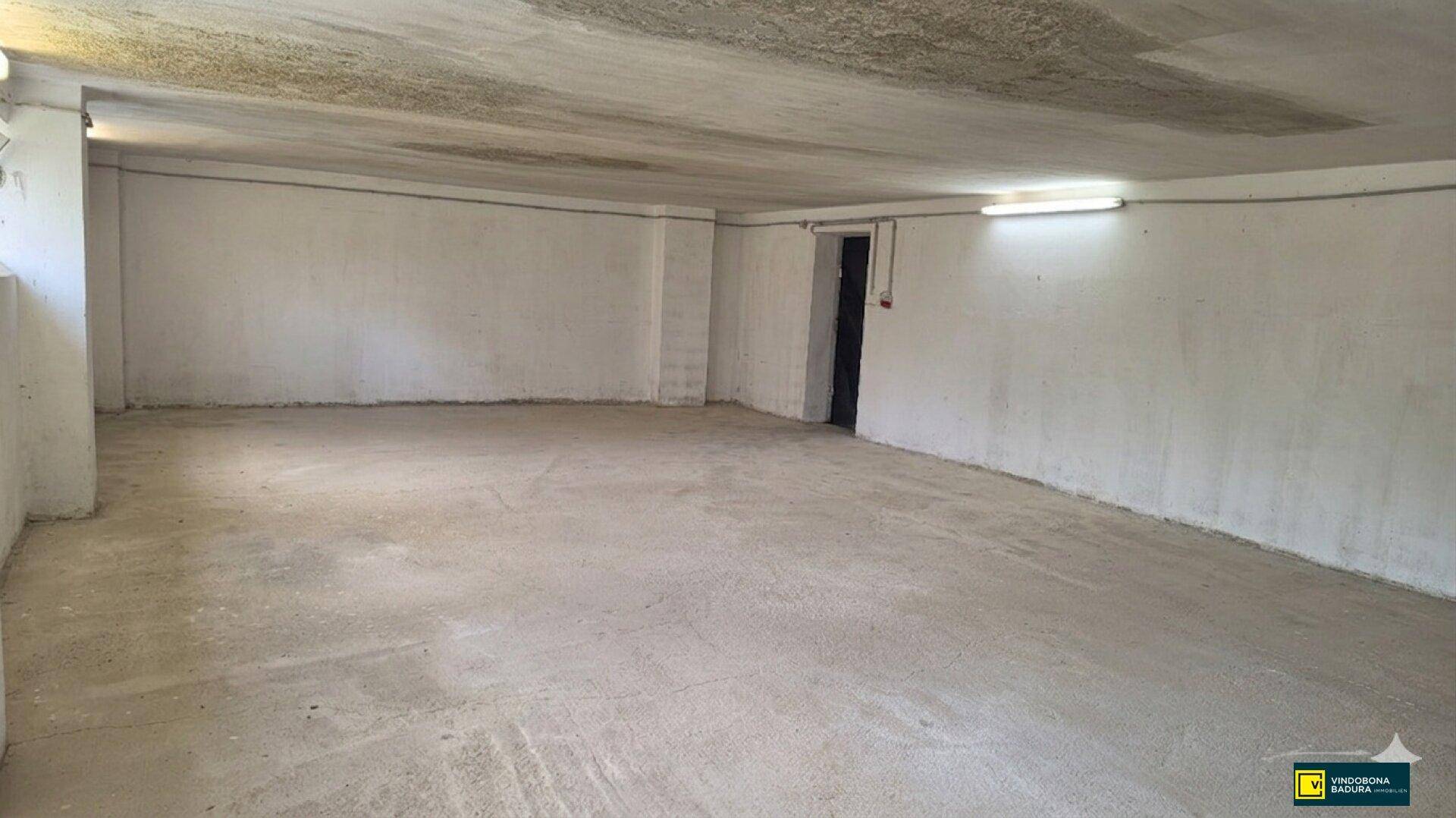 Geräumiger, leerer Innenraum mit Betonboden und weißen Wänden, beleuchtet durch Neonröhren.
