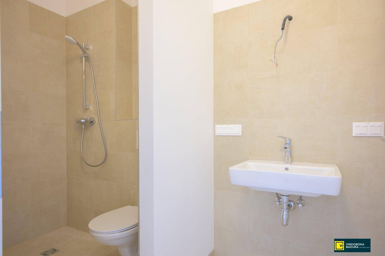 Modernes Badezimmer mit Duschbereich, Toilette und Waschbecken, komplett gefliest in Beige.