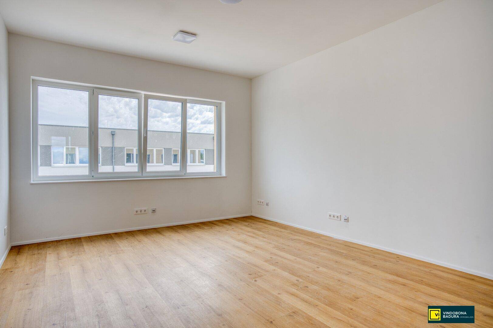 Heller, leerer Raum mit großen Fenstern und einem warmen Holzfußboden, ideal als Büro.