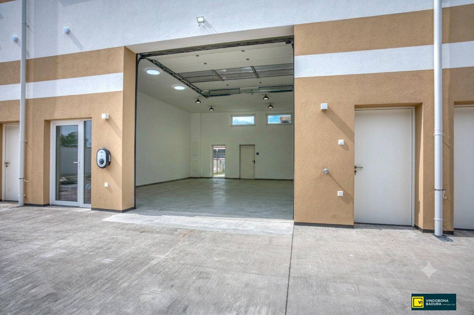 Offenes Rolltor eines Gewerberaums mit Blick ins Innere und einer Ladestation für Elektrofahrzeuge.