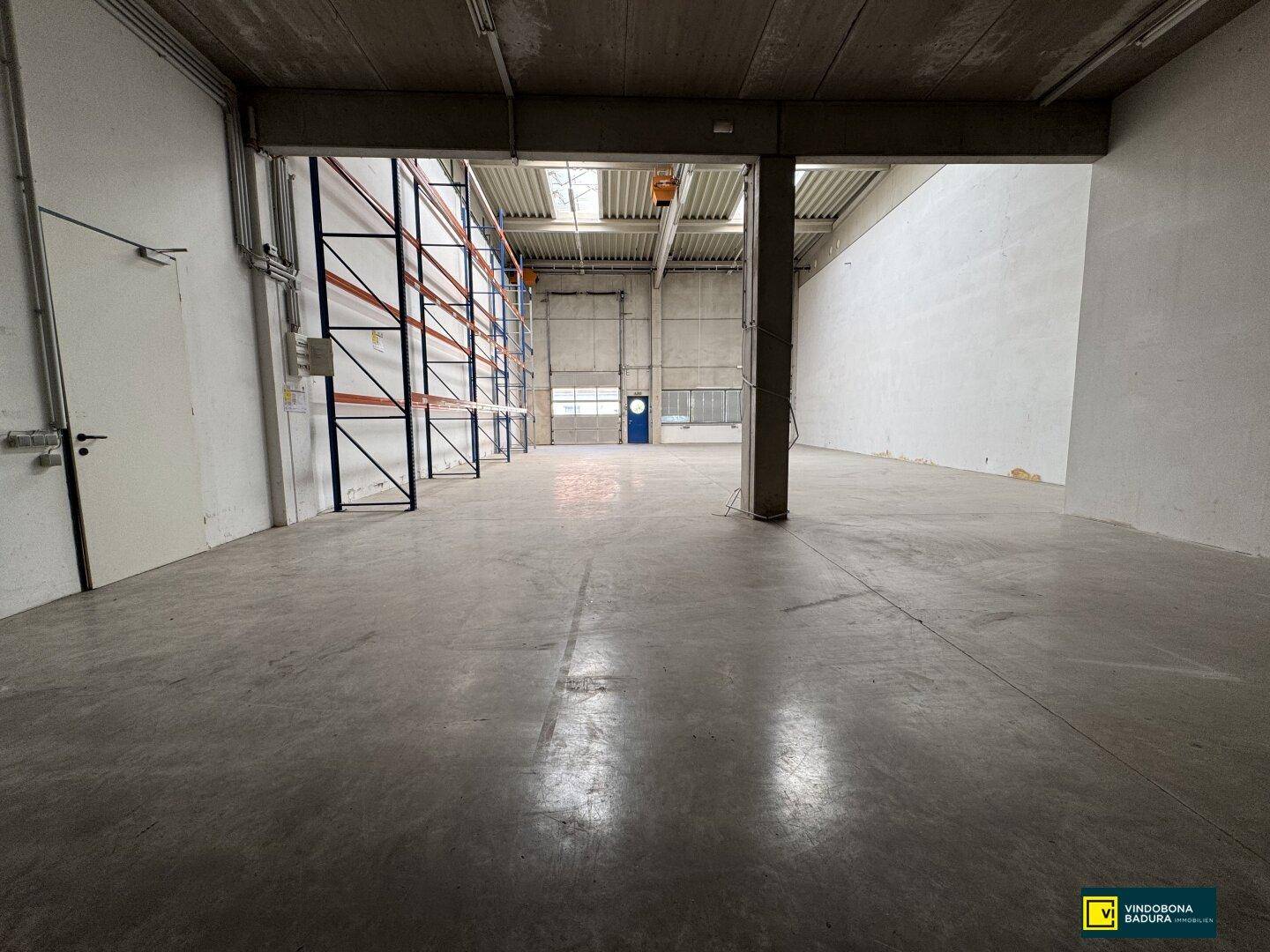 Geräumige Lagerhalle mit hohen Regalen, Betonboden und natürlicher Belichtung von oben.