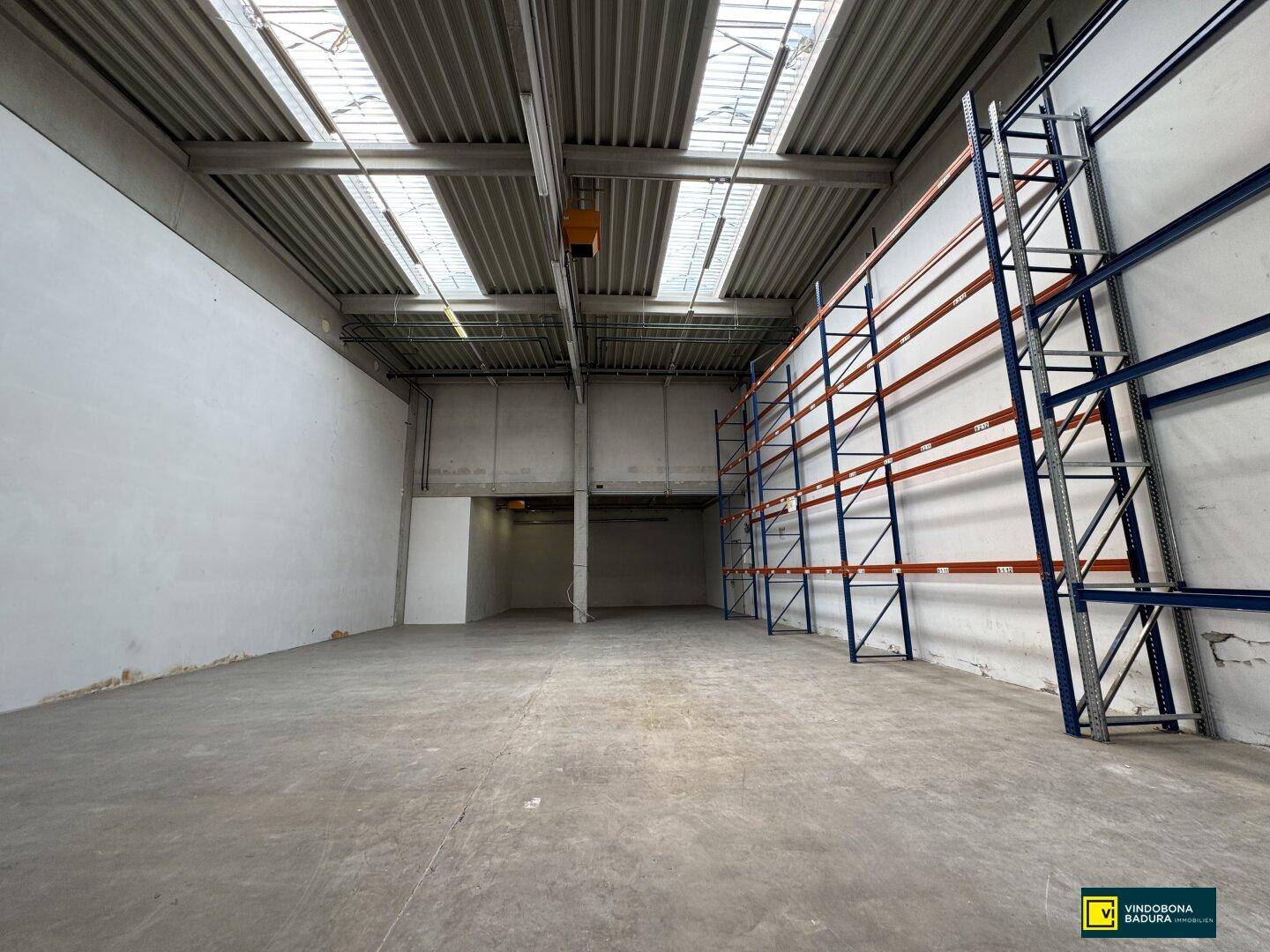 Geräumige Lagerhalle mit hohen Regalsystemen, Betonboden und Oberlichtern für Tageslicht.