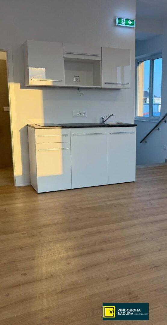 Moderne Küchenzeile mit weißen Schränken, Spüle und dunkler Arbeitsplatte in einem hellen Raum mit Holzfußboden.