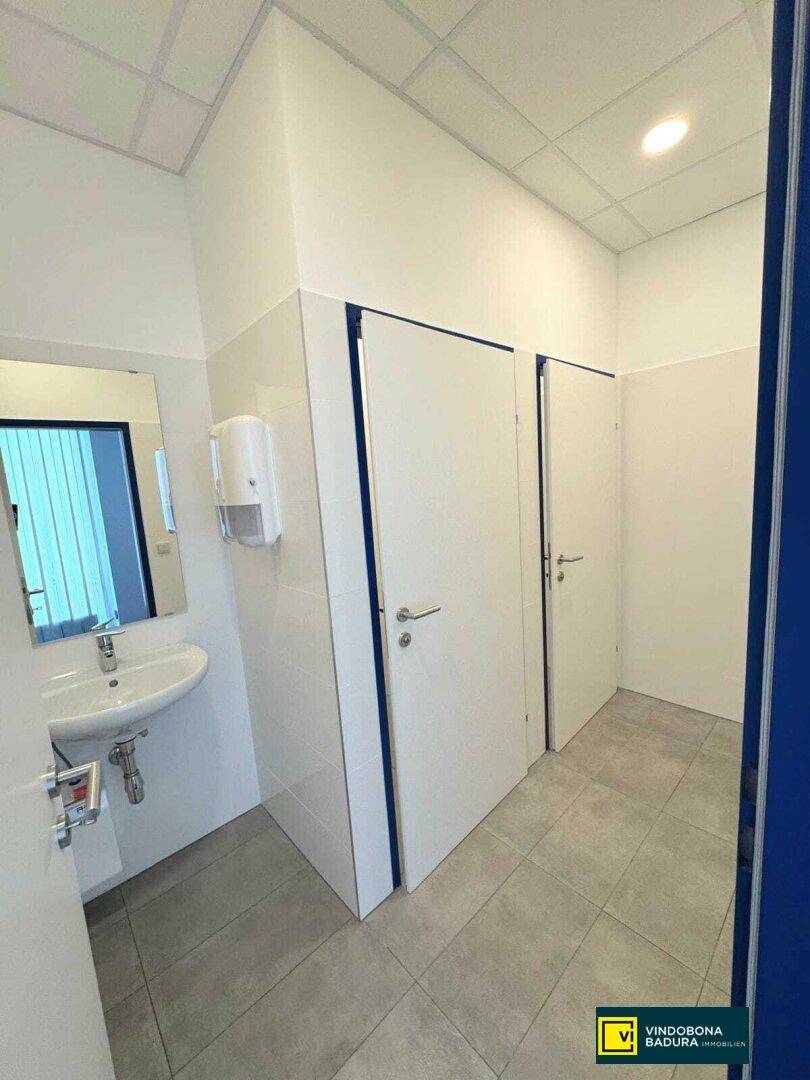 Sauberer Toilettenraum mit Waschbecken, Spiegel und gefliestem Boden.