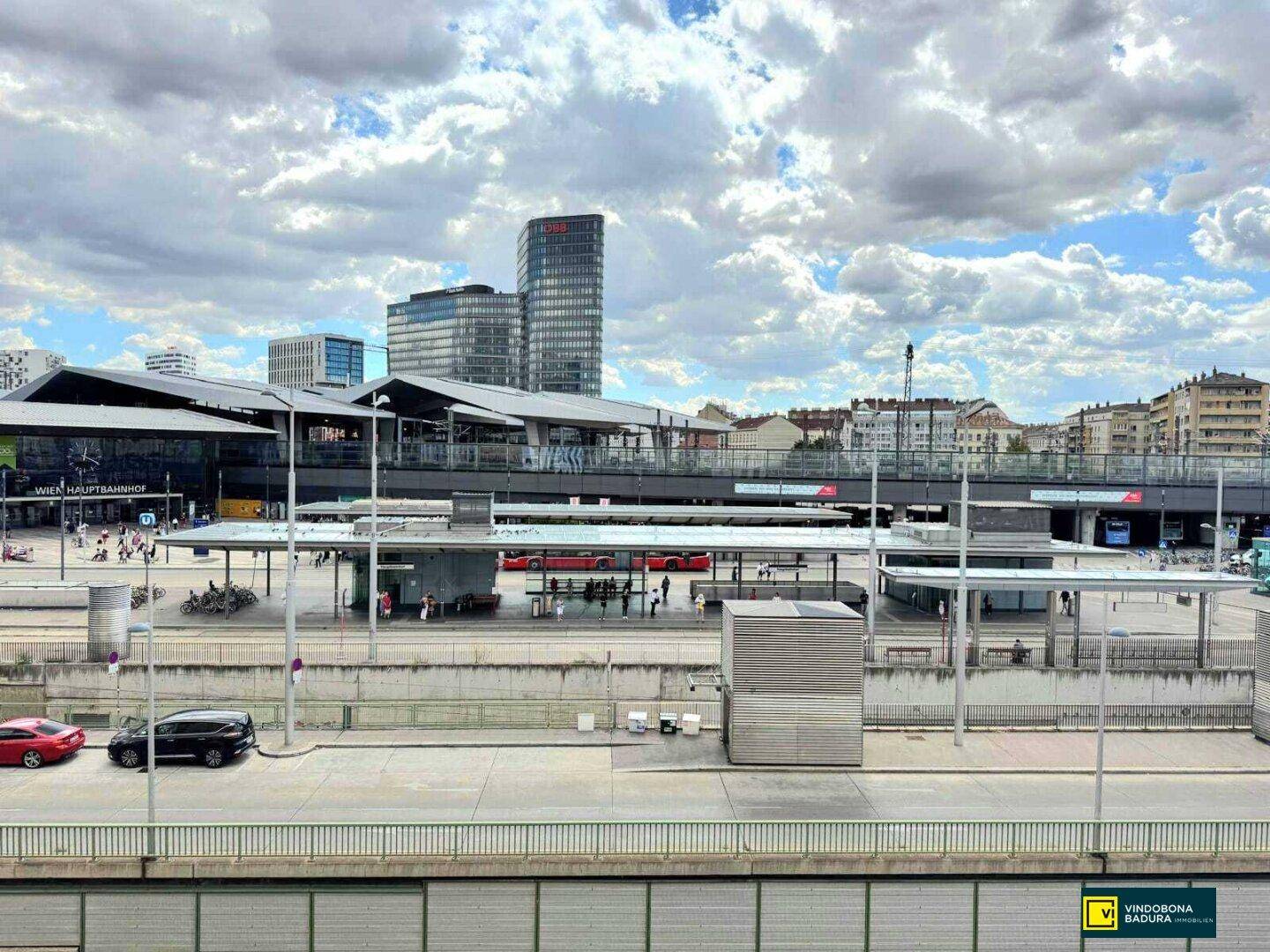 Panoramablick auf den Wiener Hauptbahnhof mit Bahnsteigen und modernen Gebäuden unter bewölktem Himmel.