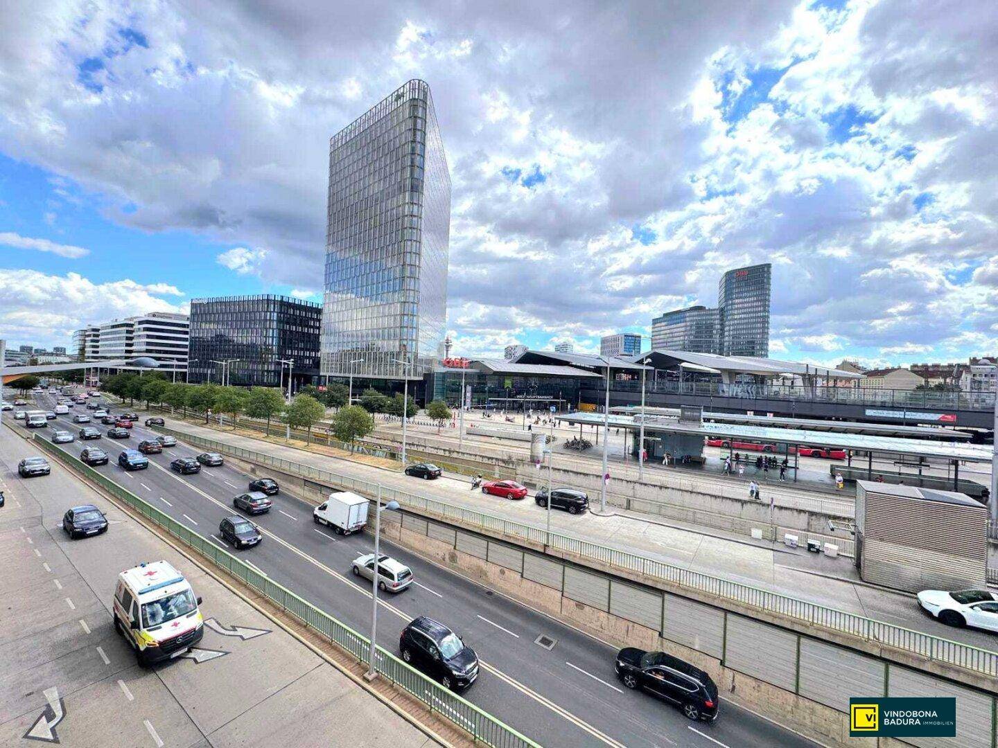 Blick auf eine belebte Stadtstraße mit modernen Glasgebäuden und dem Wiener Hauptbahnhof im Hintergrund.