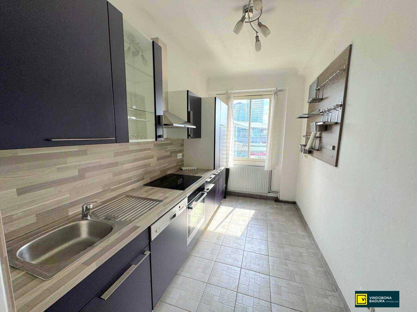 Funktionale Küche mit dunklen Schränken, Fliesenboden und Fensterblick auf die Stadt.