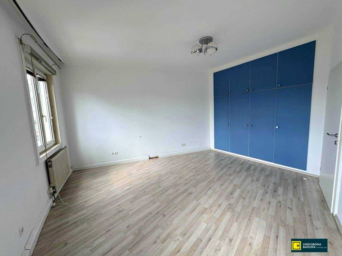 Helles Zimmer mit Laminatboden und einem großen blauen Einbauschrank an der Wand.