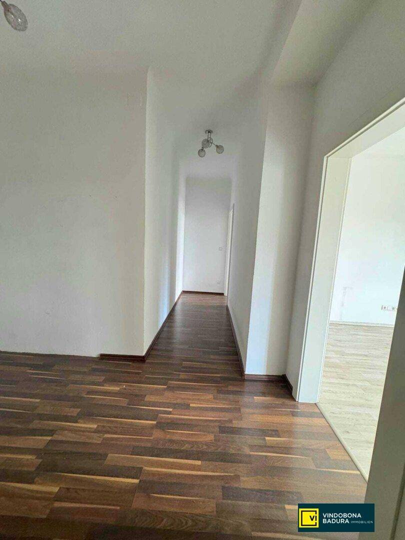 Langer, heller Flur mit dunklem Parkettboden, der zu weiteren Räumen führt.