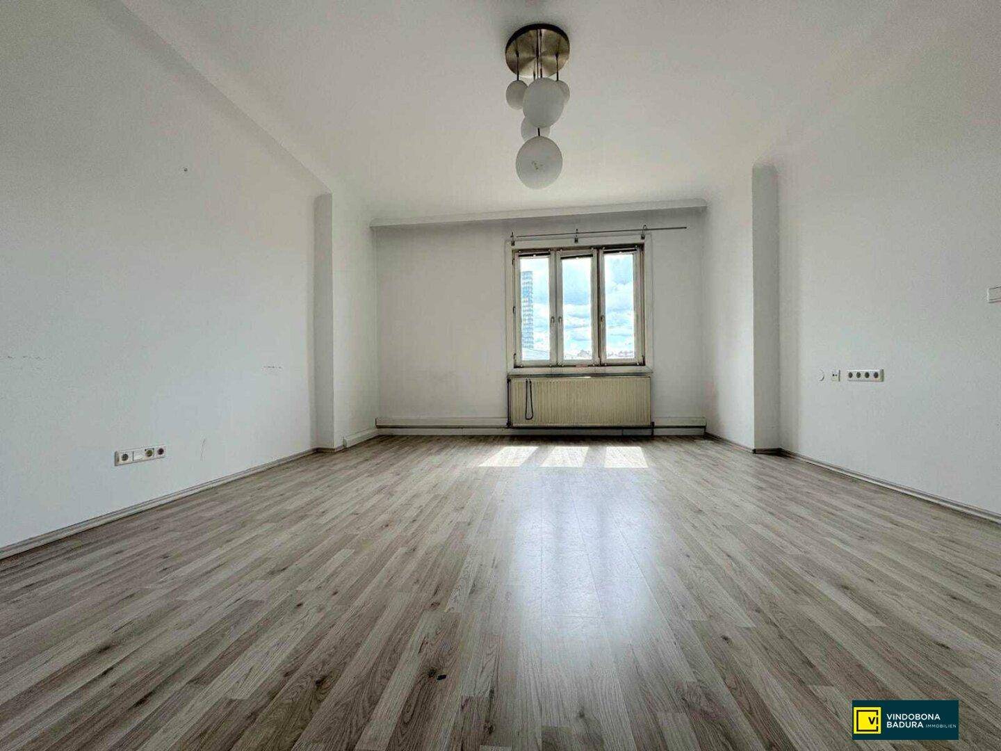 Helles und geräumiges Zimmer mit Laminatboden und einem großen Fenster.