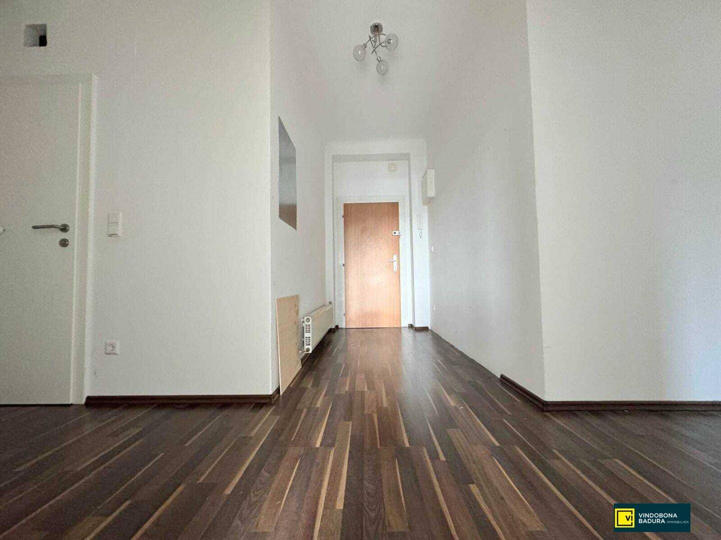 Heller Flur mit dunklem Parkettboden und einer Holztür am Ende des Ganges.
