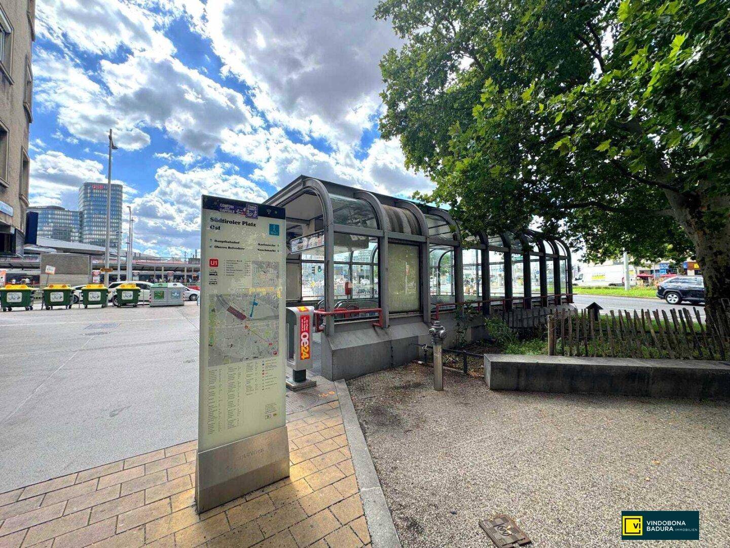 Eingang zur U-Bahn-Station Südtiroler Platz mit Bäumen und städtischer Umgebung.