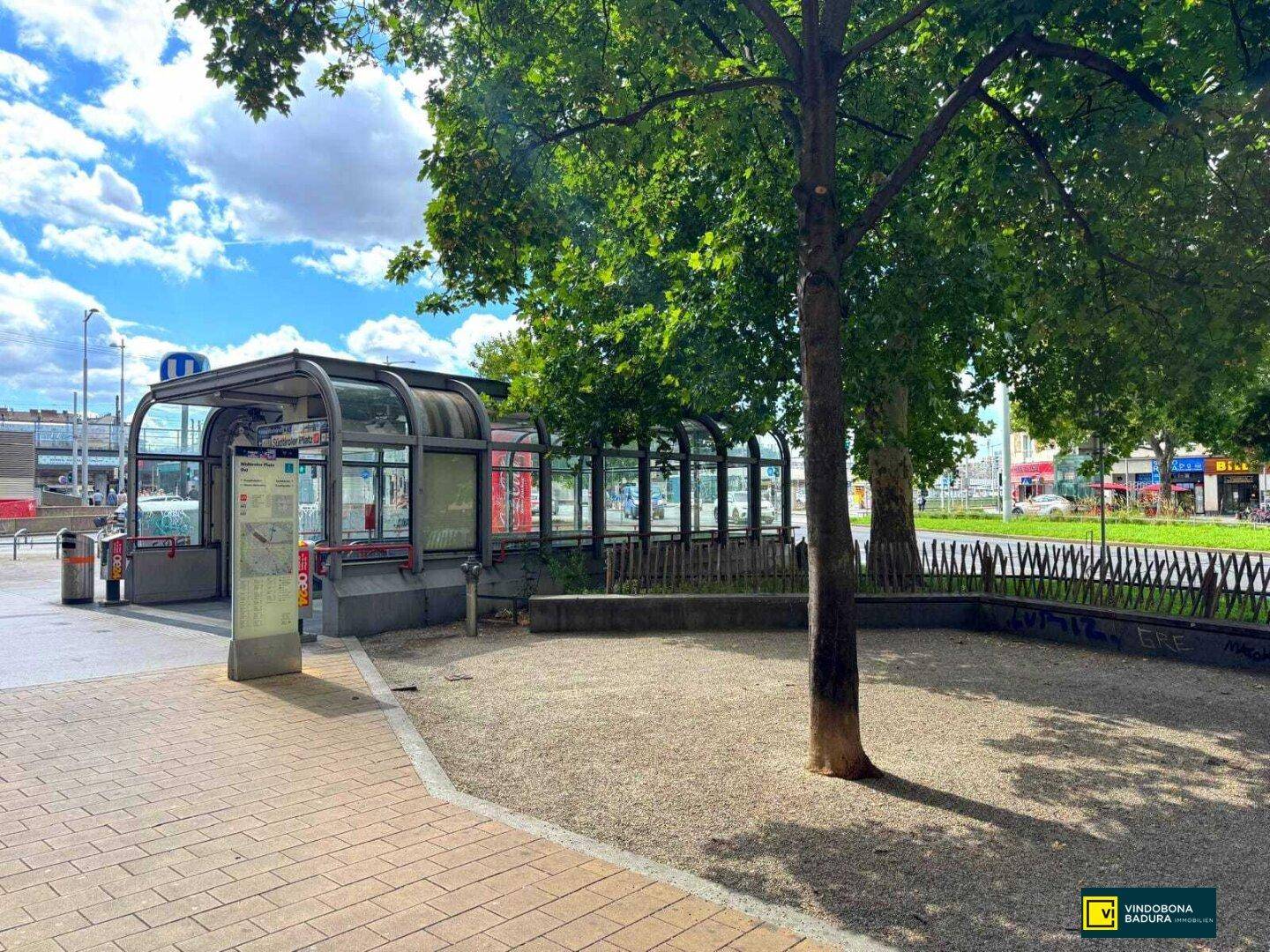 U-Bahn-Eingang umgeben von Bäumen und Grünflächen in einer städtischen Umgebung.
