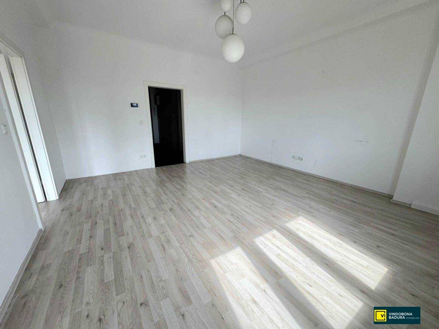 Geräumiges, helles Zimmer mit Laminatboden und einer modernen Deckenleuchte.