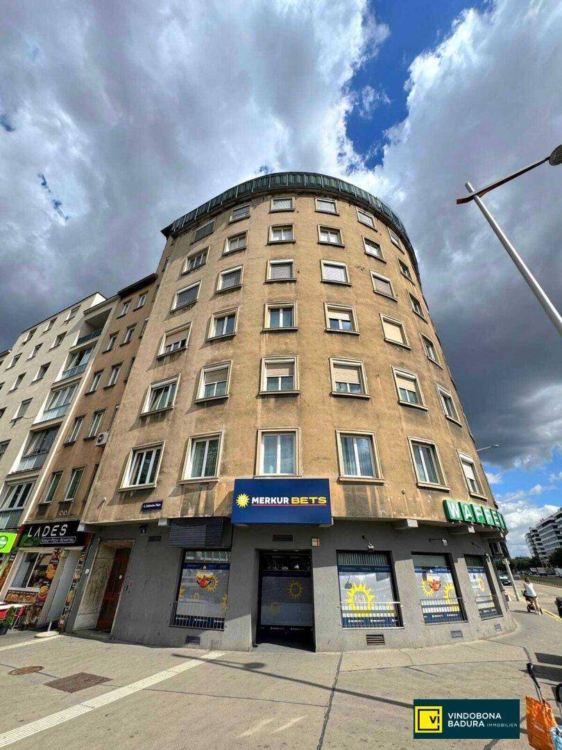 Historisches Gebäude mit runder Fassade und Geschäften im Erdgeschoss unter bewölktem Himmel.