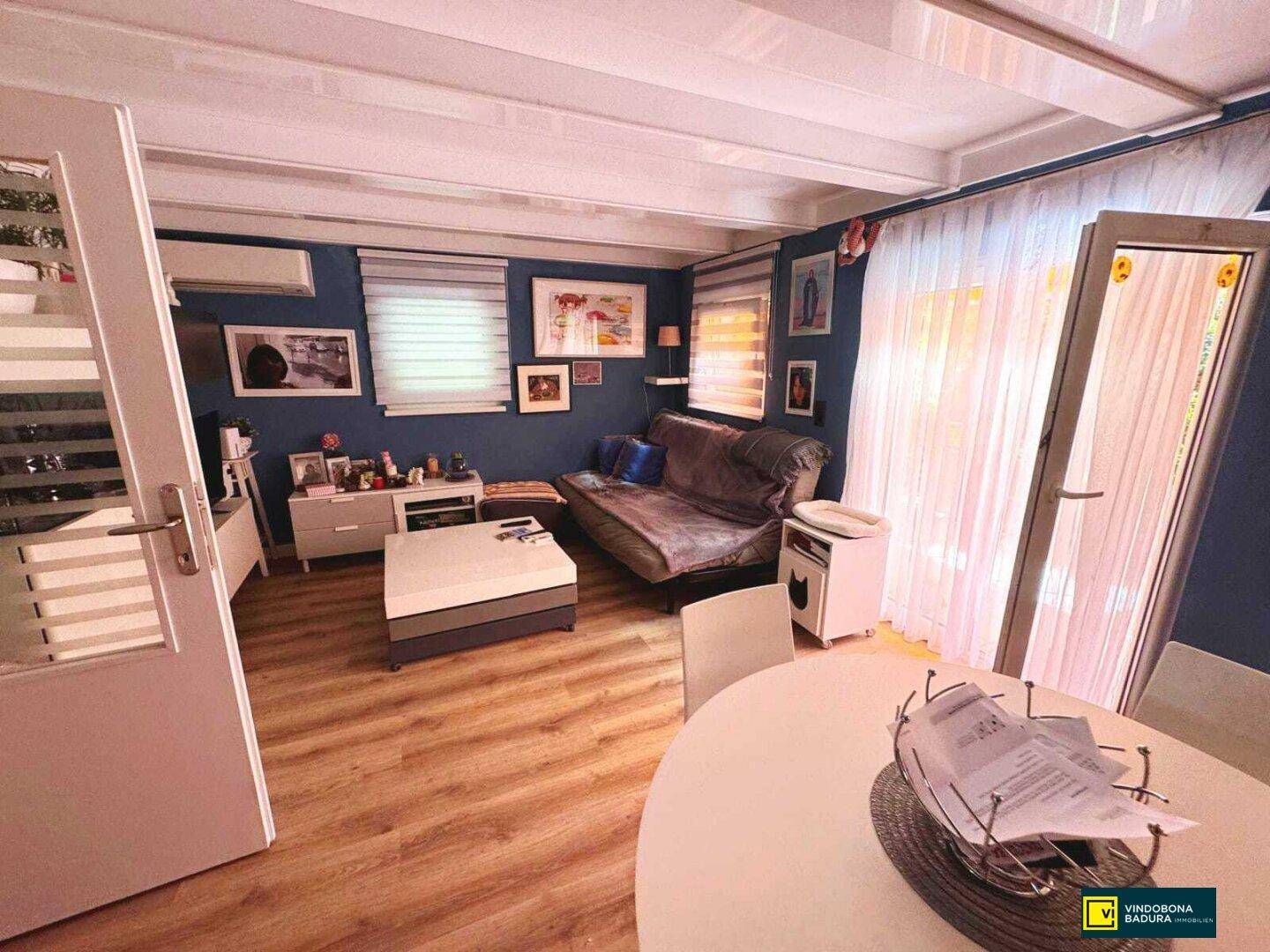 Gemütliches Wohnzimmer mit blauen Wänden, Laminatboden und Zugang zu einem Außenbereich.
