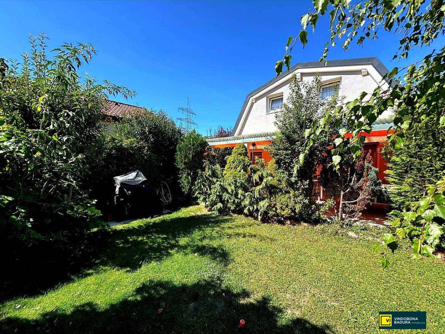 Gepflegter Garten mit Rasenfläche und vielfältiger Bepflanzung hinter dem Haus an einem sonnigen Tag.