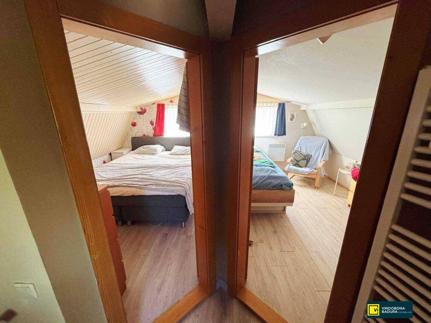 Blick durch eine Tür in zwei separate Schlafzimmer mit Dachschrägen und Laminatböden.