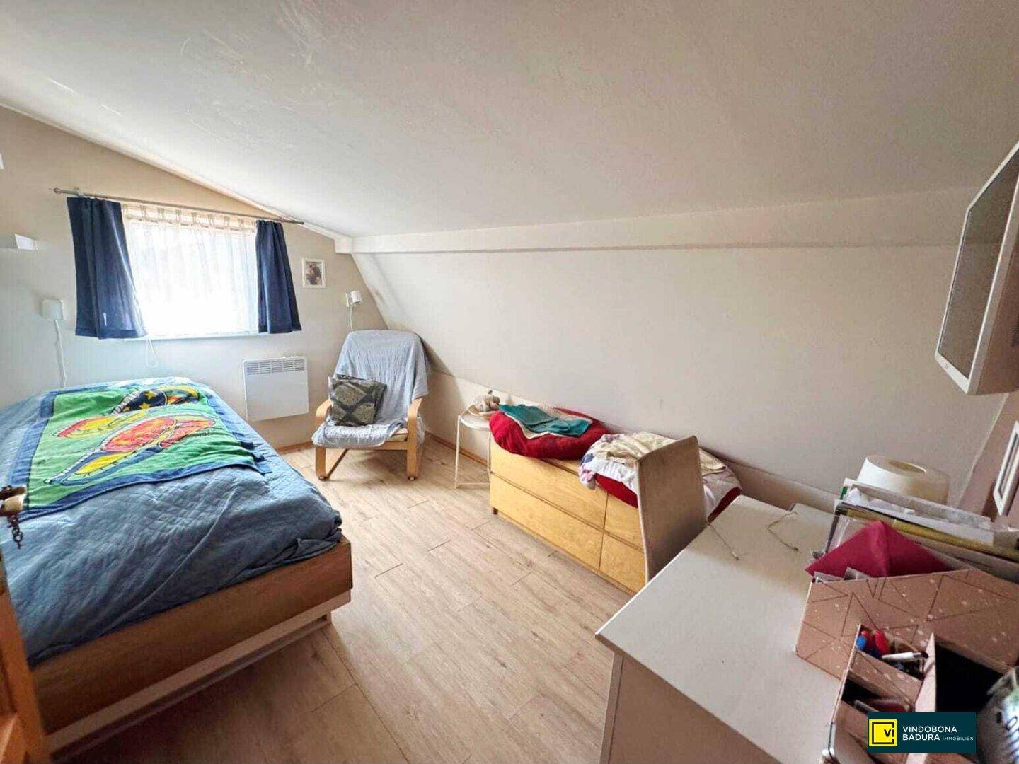 Helles Schlafzimmer im Dachgeschoss mit Einzelbett, Dachschräge und Laminatboden.