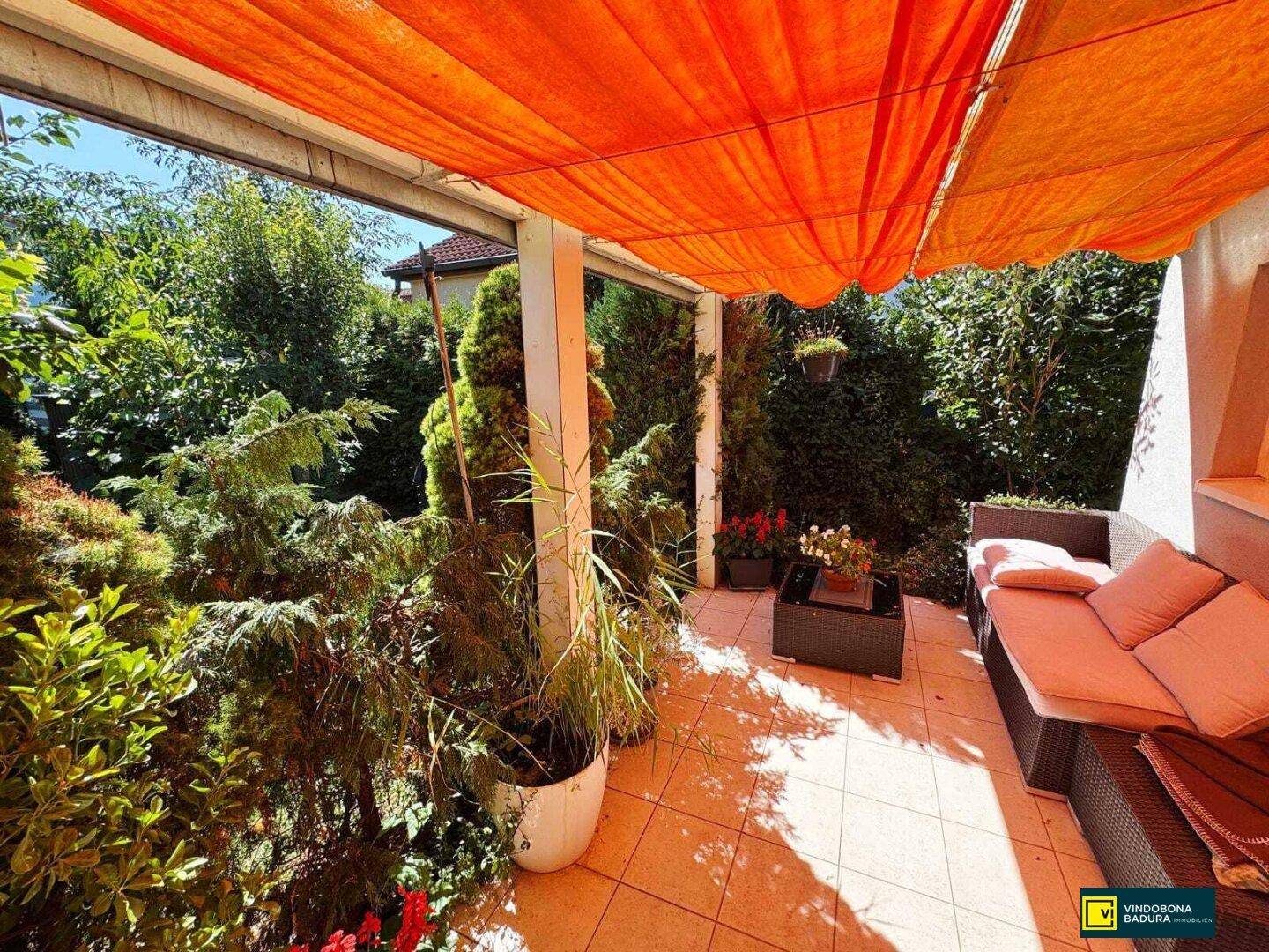 Gemütliche überdachte Terrasse mit Lounge-Möbeln und Blick ins Grüne unter einem Sonnensegel.